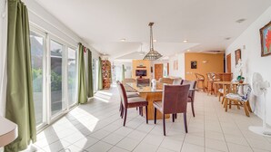 A spacious dining area with a large table and chairs, a television, and a fan. - Oceanfront Keaau Gem: Ocean & Sunrise Views, Pool (Keaau)