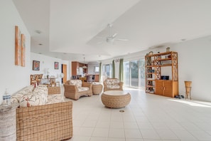 Uma sala de estar espaçosa com móveis de vime, ventilador de teto e uma grande janela com cortinas.