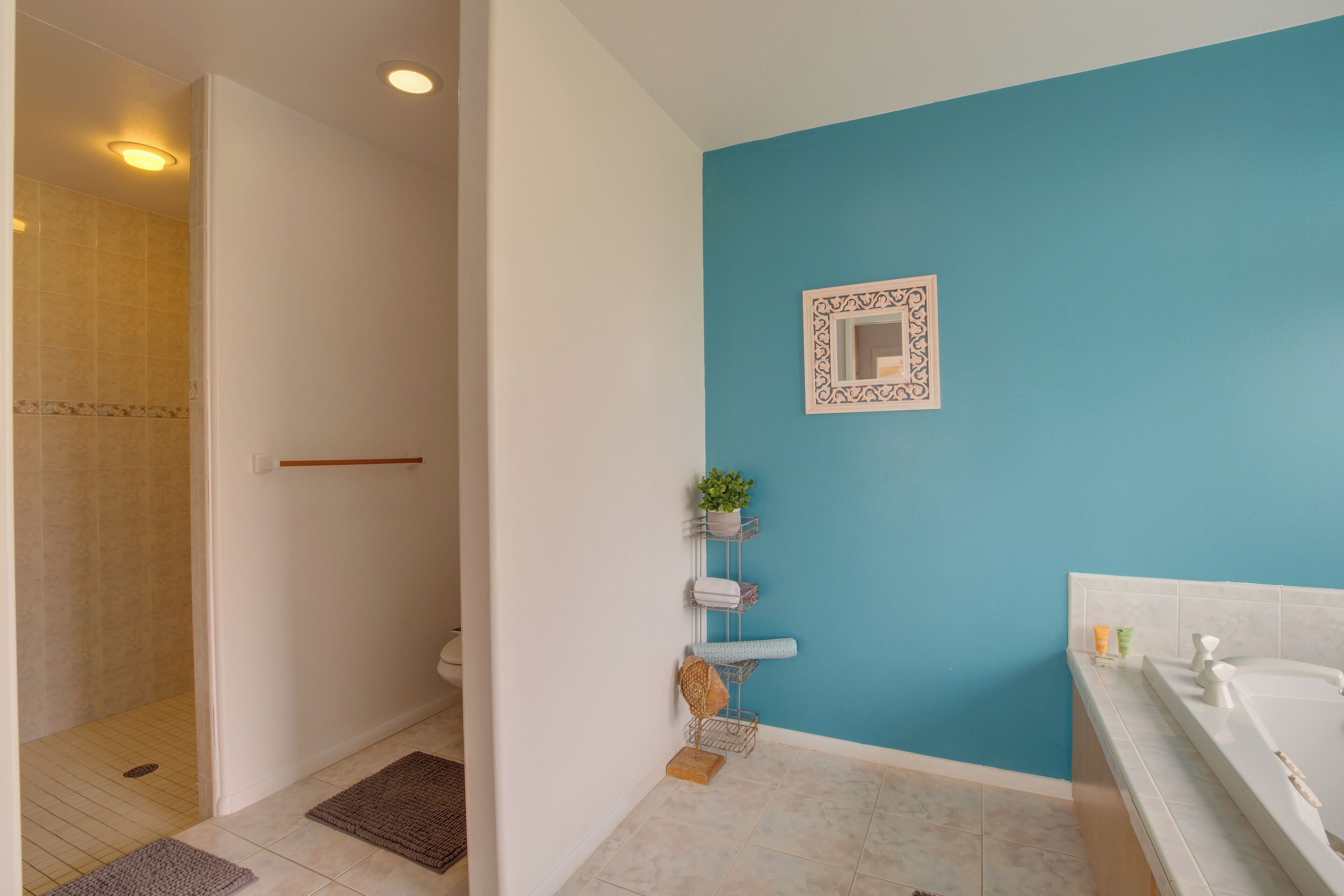 A bathroom with a blue wall, a white bathtub, a shower area, and a shelf with toiletries.
