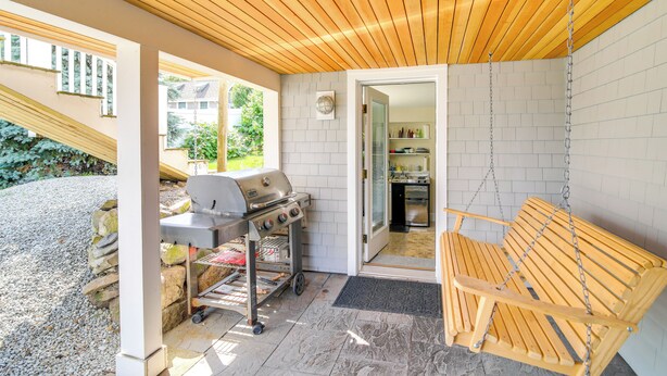 An outdoor patio with a wooden ceiling, a grill, a hanging wooden swing, and a view of a kitchen through an open door. - Pet-friendly Garden Studio ~ 25 Mi to Boston! (Scituate)