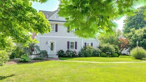 A white house with purple shutters, surrounded by a well-maintained lawn and various shrubs. - Pet-friendly Garden Studio ~ 25 Mi to Boston! (Scituate)