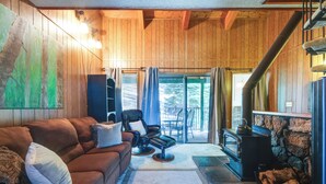 Una sala de estar acogedora con un sofá marrón, un sillón de cuero negro, una chimenea de piedra y un techo de madera.