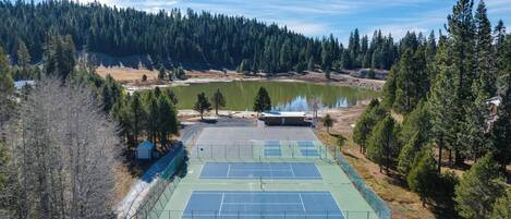 Un court de tennis en plein air, entouré d’arbres et bordé d’un lac.