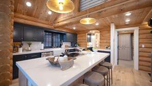 A modern log cabin kitchen with a large island, dark cabinets, and wooden ceiling beams. - Ogden's Fancy Fly Luxury Teton Springs Cabin in Victor, ID w/ A/C & Hot Tub (Victor)