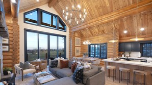 A spacious log cabin interior with a large living area, a kitchen with bar stools, and large windows offering views of the outdoors. - Ogden's Fancy Fly Luxury Teton Springs Cabin in Victor, ID w/ A/C & Hot Tub (Victor)