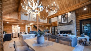 A spacious log cabin interior with a central dining table, a fireplace, and a mezzanine level. - Ogden's Fancy Fly Luxury Teton Springs Cabin in Victor, ID w/ A/C & Hot Tub (Victor)