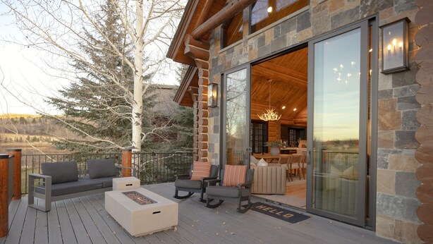 A wooden deck with outdoor seating, a fire pit, and a view of the interior through a glass door. - Ogden's Fancy Fly Luxury Teton Springs Cabin in Victor, ID w/ A/C & Hot Tub (Victor)