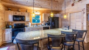 A wooden cabin kitchen with granite countertops, a central island with bar stools, and hanging pendant lights. - Majestic Views-Hot Tub - Views - Gas Firepit -4WD-AWD (Whittier)