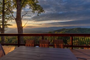 A wooden deck with a table and chairs, overlooking a mountainous landscape with a sunset. - Majestic Views-Hot Tub - Views - Gas Firepit -4WD-AWD (Whittier)