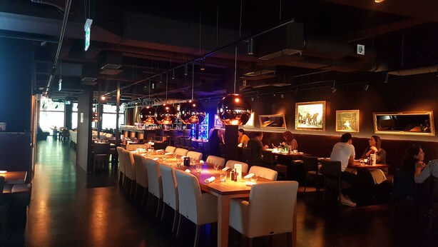 A restaurant with long communal tables, individual booths, and hanging pendant lights.