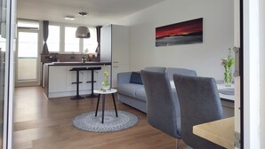 A modern living room with a grey sofa, a round coffee table, and a dining area with a kitchen in the background.