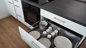 A kitchen with a black countertop, white cabinets, and a drawer with patterned bowls and cups.