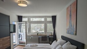A modern hotel room with a large bed, a desk, and a window with blinds.