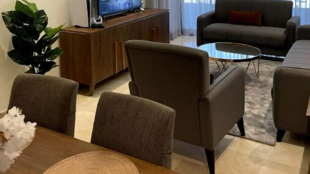 Un salon moderne doté d’un téléviseur à écran plat, de sièges confortables et d’une grande fenêtre offrant une vue sur la ville.