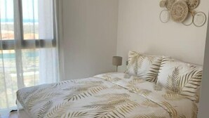 Une chambre à coucher comprenant un lit, une table de chevet, une lampe fixée au mur et une vue sur l’extérieur par une fenêtre agrémentée de rideaux.