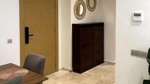 Une pièce avec une porte en bois, un buffet en bois sombre, une petite table avec une chaise et un sol carrelé.