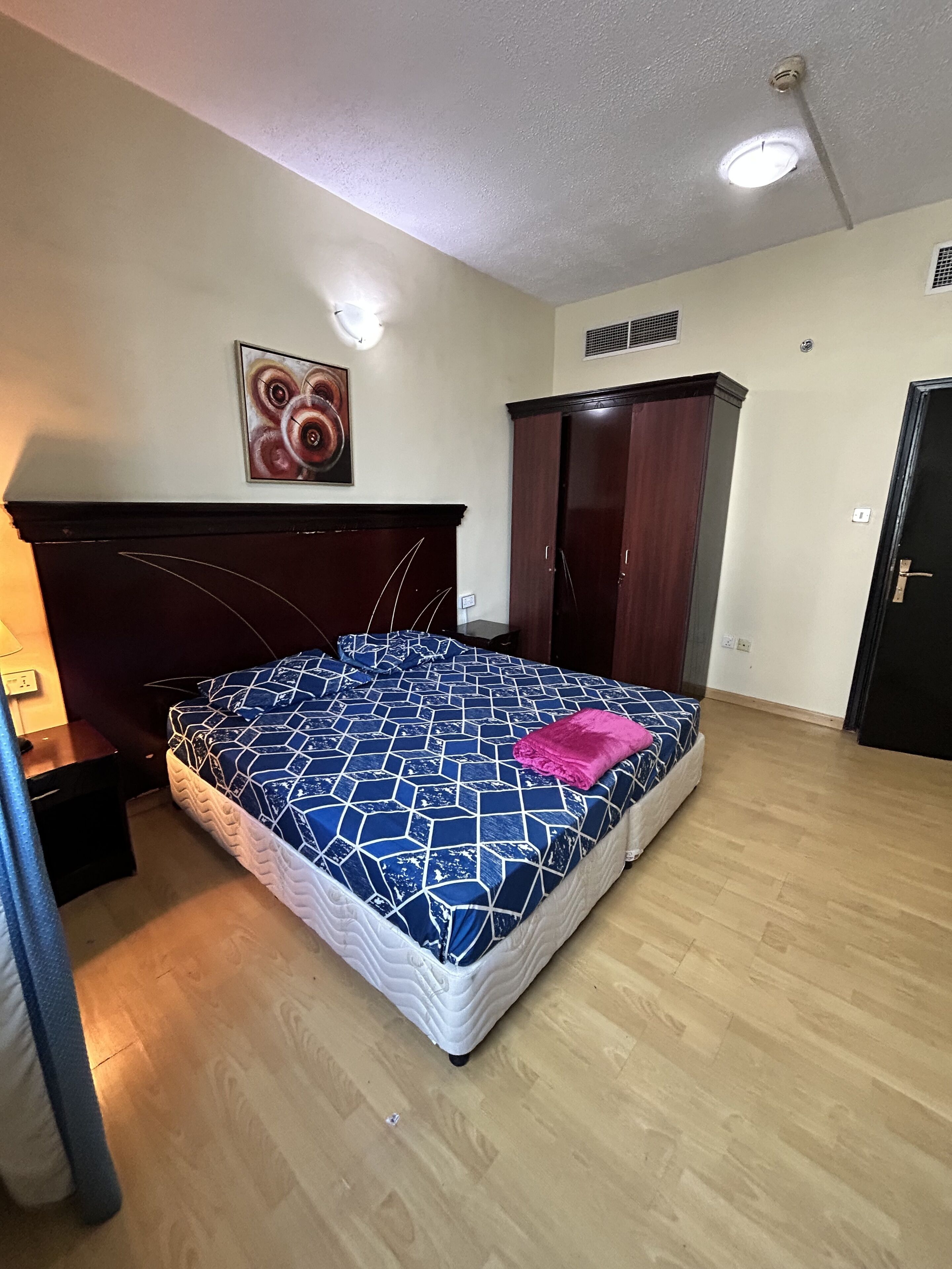 Une chambre à coucher avec un lit, une table de chevet, une armoire et un tableau au mur.