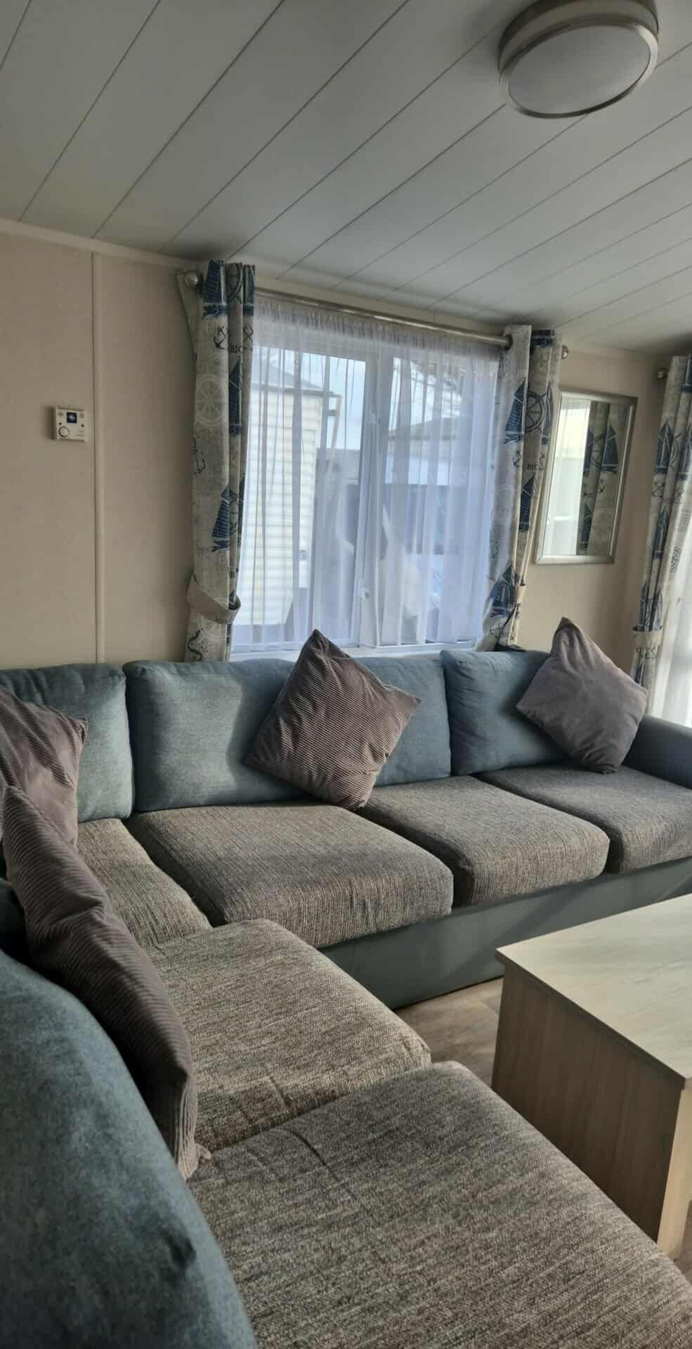 A modern living room with a sectional sofa, a coffee table, and a window with curtains.