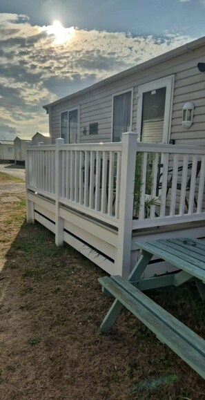Une maison mobile à l’extérieur blanc, dotée d’une terrasse clôturée et d’une table de pique-nique.