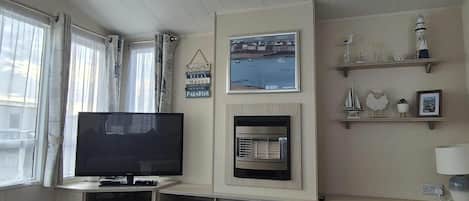 A living room with a flat-screen TV, a fireplace, and a view of the sea.