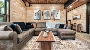 Un salon chaleureux avec un plafond en bois, un canapé d’angle, une table basse et des œuvres d’art accrochées aux murs.