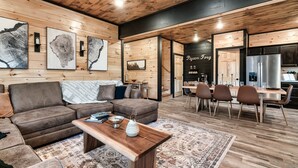Un salon moderne avec un plafond en bois, un canapé d’angle, une table basse et un coin repas avec des chaises.