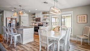 A modern kitchen with white cabinetry, a central island, and pendant lighting. - `Charming Cabin with Private Pool & Spacious Veranda, Steps from Town and Beach!` (Port Aransas)