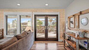 A modern living room with a large sofa, a wooden coffee table, and a view of a balcony with outdoor furniture. - `Charming Cabin with Private Pool & Spacious Veranda, Steps from Town and Beach!` (Port Aransas)