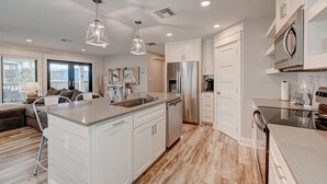 A modern kitchen with white cabinetry, stainless steel appliances, and a central island. - `Charming Cabin with Private Pool & Spacious Veranda, Steps from Town and Beach!` (Port Aransas)