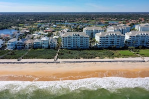 Un hôtel en bord de mer composé de plusieurs bâtiments, doté d’une plage de sable et offrant une vue sur le quartier résidentiel environnant.