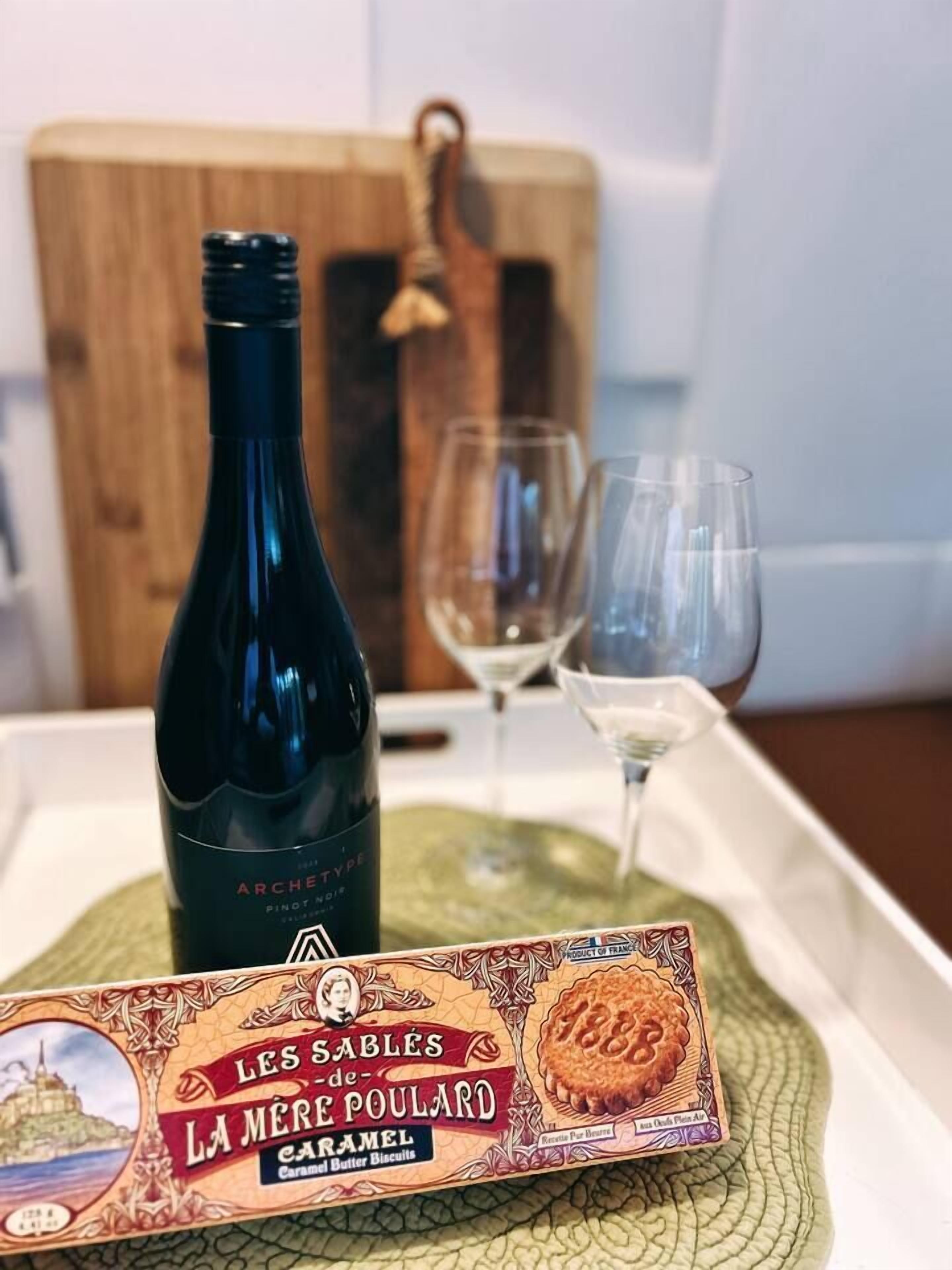 A bottle of wine, two glasses, and a box of Les Sables de La Mere Poulard caramel butter biscuits on a tray.