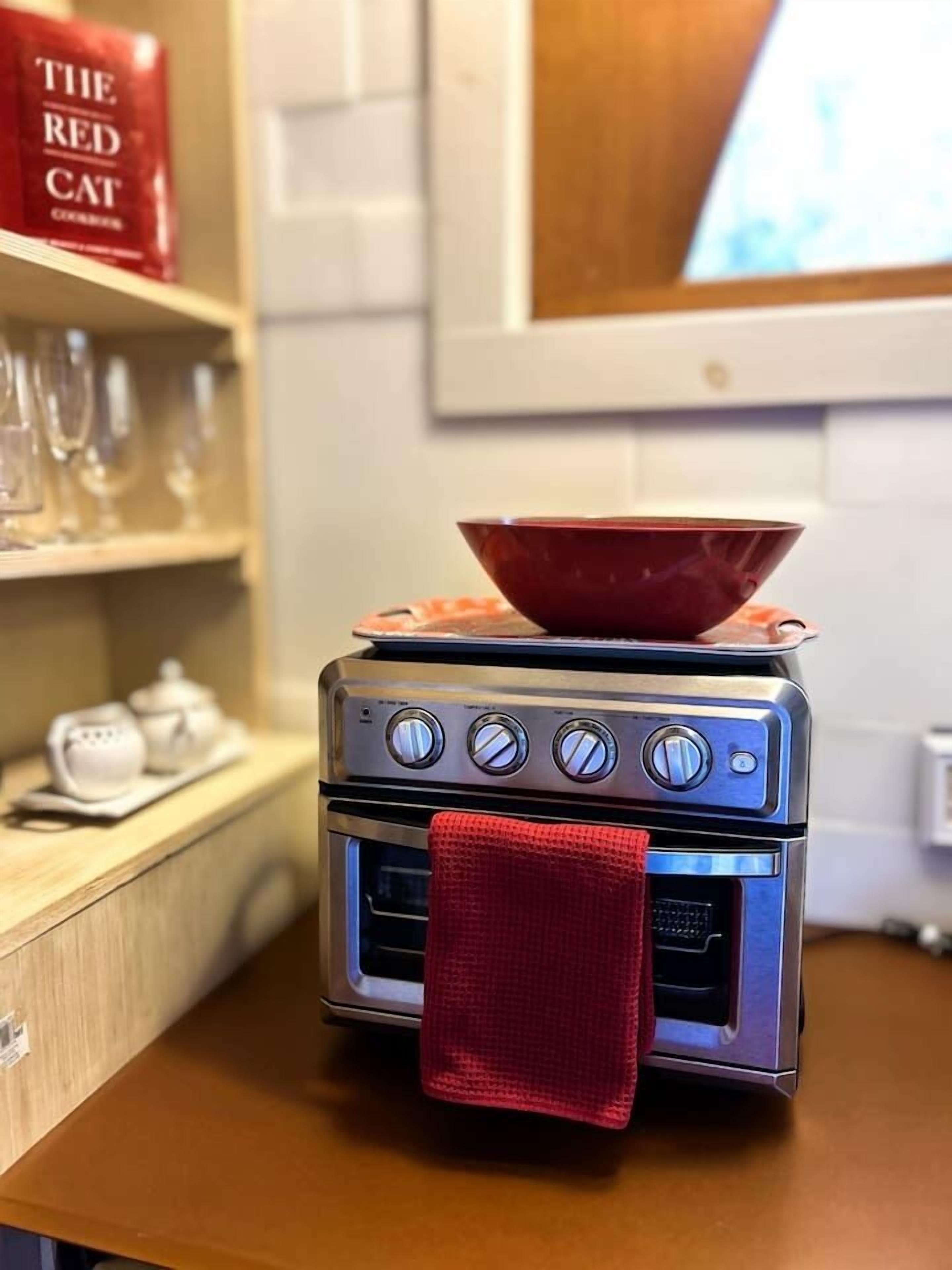 A compact kitchen with a small stove, a red bowl on top, and a red towel hanging from the oven door.