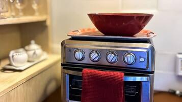 A compact kitchen with a small stove, a red bowl on top, and a red towel hanging from the oven door.