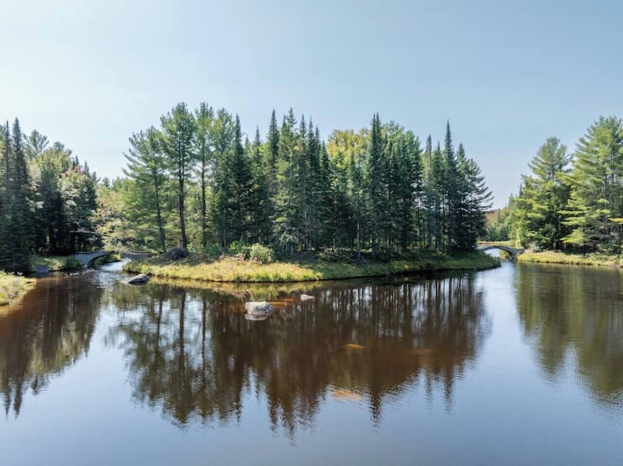 A calm lake surrounded by dense forest and a small bridge.