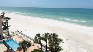 Blick auf einen Strand mit Poolbereich, Palmen und blauem Himmel.
