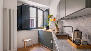 Une cuisine de taille réduite, avec une fenêtre, un radiateur, un tabouret en bois et un plan de travail en marbre.