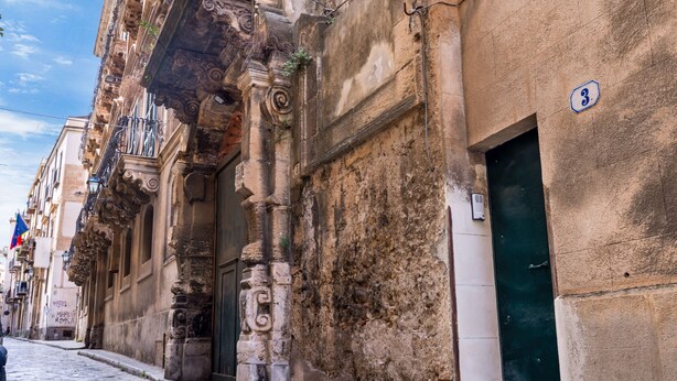Une ruelle pavée étroite bordée de bâtiments historiques, caractérisés par leurs balcons richement décorés et leur façade en pierre.