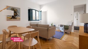 Un salon moderne avec un canapé, une table à manger et des chaises, ainsi qu’une grande fenêtre.
