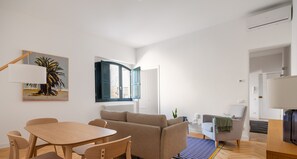 Ein modernes Wohnzimmer mit einer Couch, einem Esstisch mit Stühlen und einem großen Fenster.