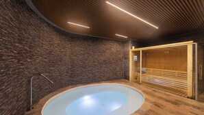 Un espace spa comprenant un grand jacuzzi circulaire, un sauna en bois et un mur en briques.