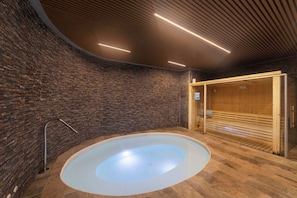A spa area with a large circular hot tub, wooden sauna, and a brick wall.