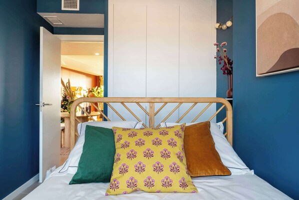 A bed with a wooden headboard, a yellow pillow with a floral pattern, a green pillow, and a brown pillow.