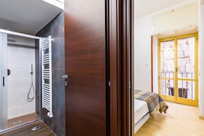 Ein Schlafzimmer mit Bett, einer Holztür, einem Badezimmer mit Dusche und einem Balkon mit Blick.