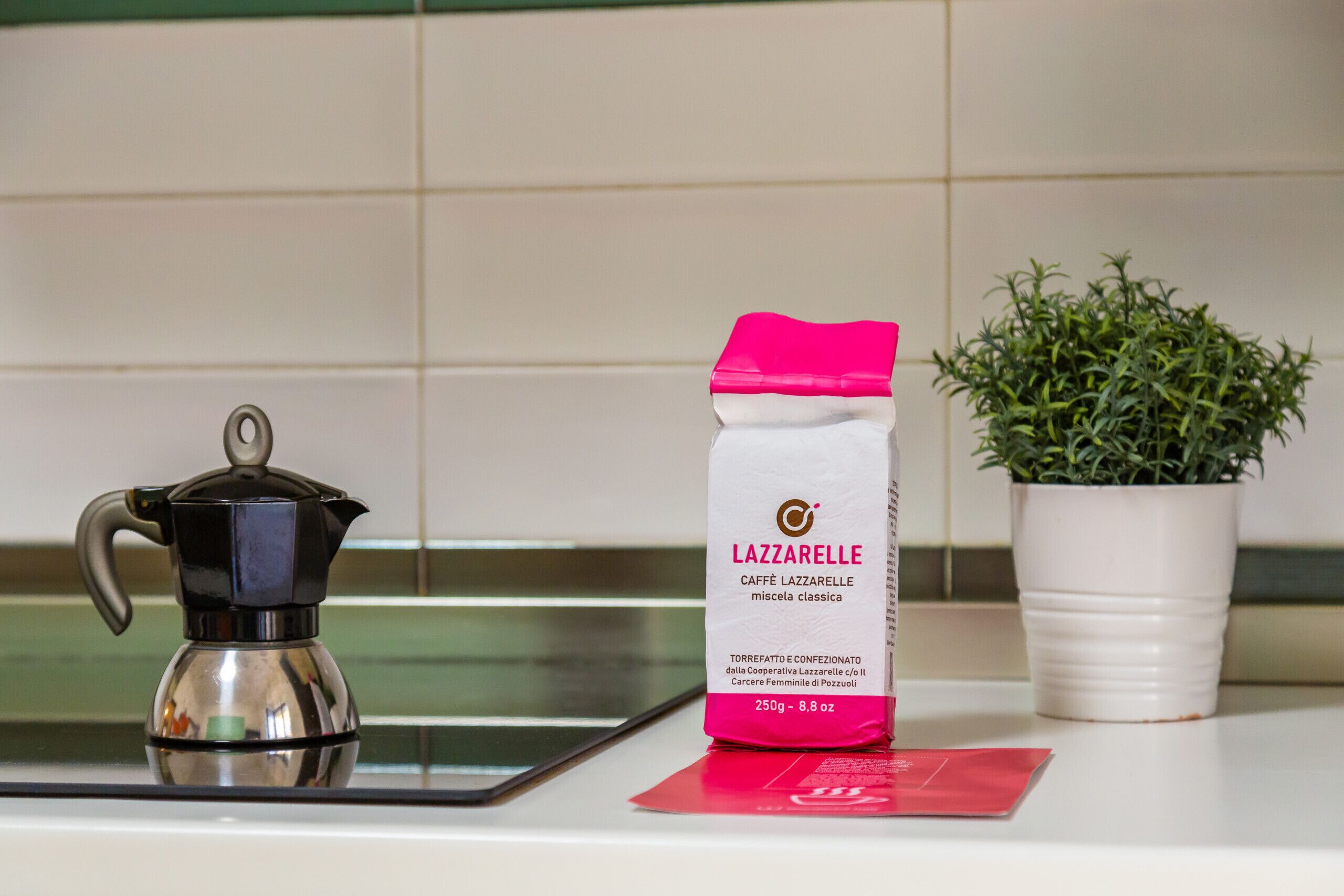 Een aanrecht met een koffiezetapparaat, een pak Lazzarelle koffie en een potplant.