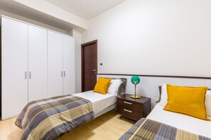 Un dormitorio con dos camas, un armario, una mesita de noche con lámpara y una puerta.