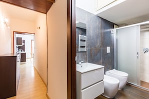 Ein modernes Badezimmer mit Duschkabine aus Glas, einem weißen Waschbecken und zwei Toiletten.