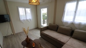 En stue med sofa, et lille bord med en vase og et fjernsyn monteret på væggen.