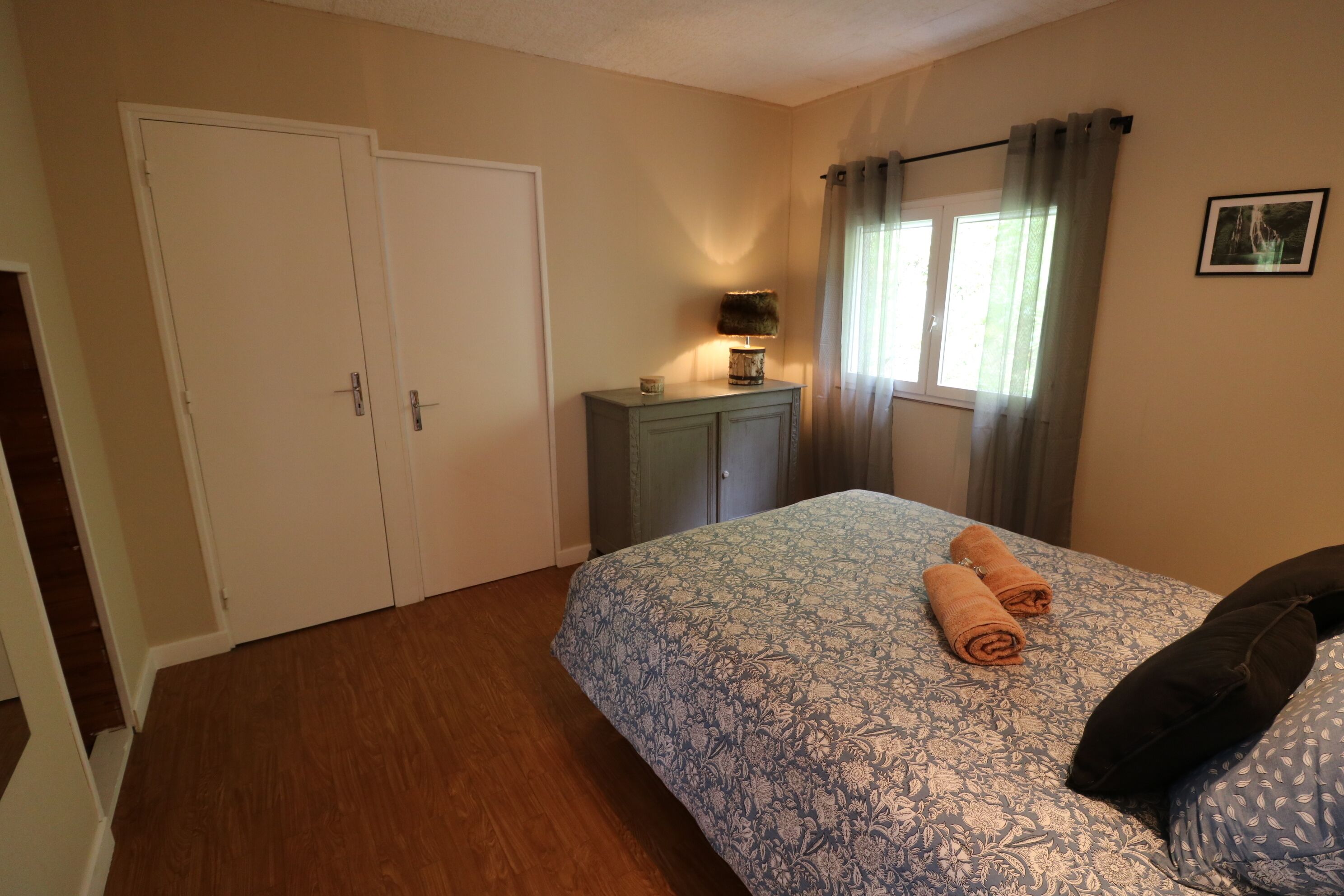 A bedroom with a bed, a dresser, a lamp, a window with curtains, and a door.
