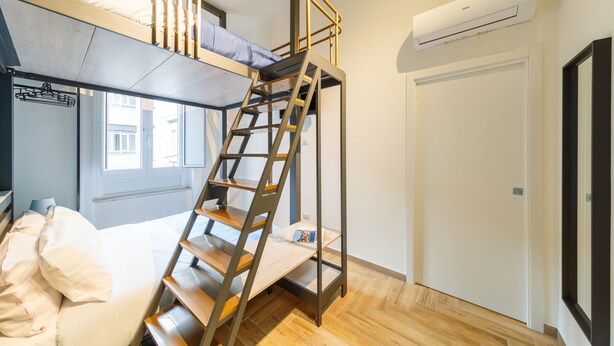 A dorm-style room with a bunk bed, a wooden ladder, a window, and an air conditioning unit. - Central Station Apts by Wonderful Italy - Cetara (Napoli)