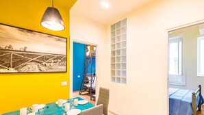 A dining area with a blue table set for four, a ladder leading to a blue door, and a bed with a blue bedspread in the adjacent room. - Central Station Apts by Wonderful Italy - Cetara (Napoli)